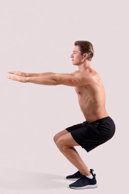 Gövdesi çıplak atletik bir adamın hafif stüdyo arkaplanı üzerinde aerobik egzersizleri yaparken yandan görünüşü.
