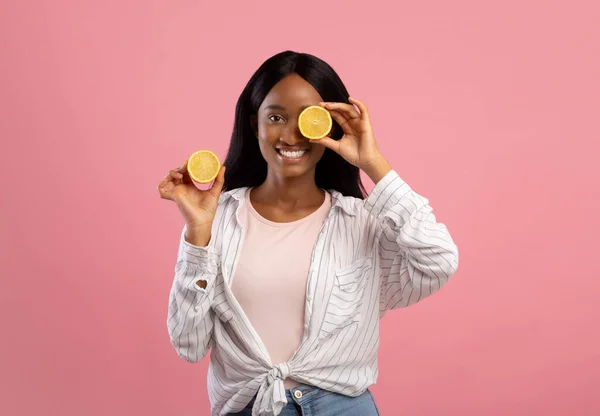 Vitaminas de fruto de cuidados com a pele. Senhora preta atraente cobrindo seu olho com limão cortado no fundo do estúdio rosa — Fotografia de Stock