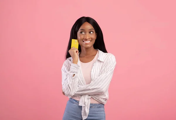 Retrato de senhora afro-americana pensativa com cartão de crédito recomendando serviços bancários em fundo de estúdio rosa — Fotografia de Stock