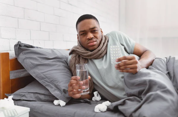 Hombre africano enfermo mostrando píldoras de la medicina acostado en la cama interior — Foto de Stock