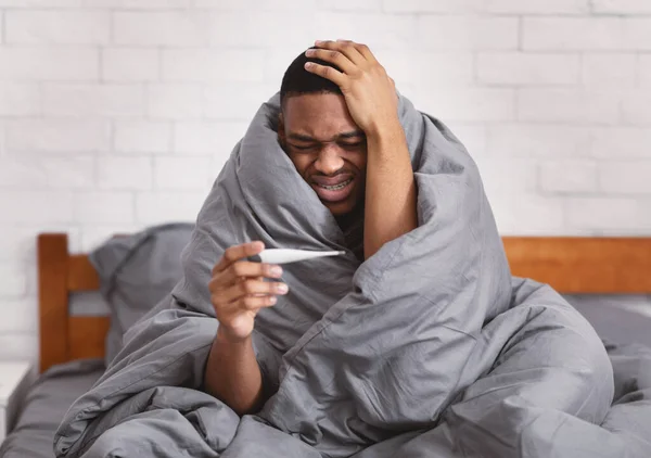 Homem negro doente com febre sentado na cama em casa — Fotografia de Stock