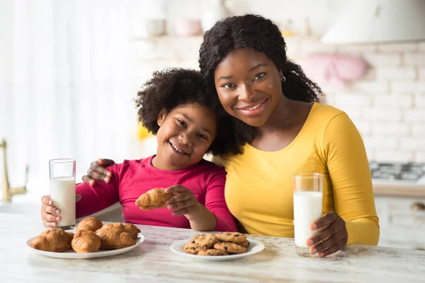 Czarna matka i córeczka jedzą ciasteczka i piją mleko w kuchni — Zdjęcie stockowe