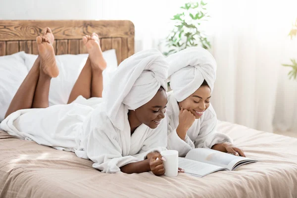 Twee ontspannen Afro-Amerikaanse dames drinken thee en lezen tijdschrift — Stockfoto