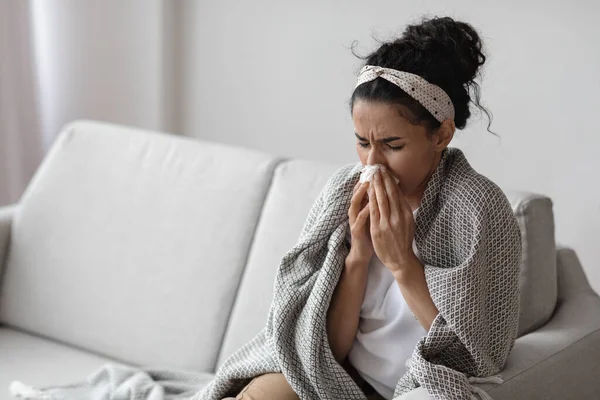 Sick young woman wrapped in blanket sneezing, home interior — Stock Photo, Image