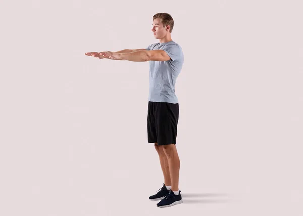 Sterke millennial guy doet squats oefeningen op lichte studio achtergrond, volledige lengte portret — Stockfoto