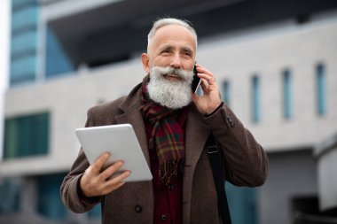 Sokakta yürürken telefonda konuşan yakışıklı, gri saçlı adam.
