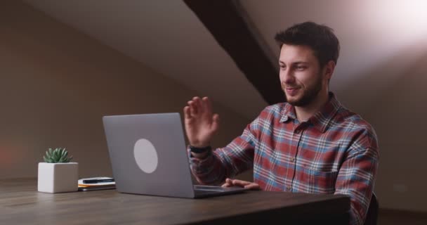 年轻人坐在总公司的办公室里，一边向笔记本电脑屏幕挥手告别，一边关上笔记本电脑 — 图库视频影像