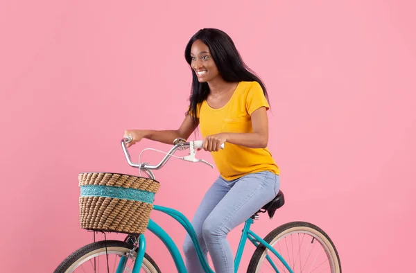 Portrait of pretty African American lady riding vintage bike over pink studio background — Stock Photo, Image