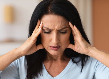 Olgun esmer kadın şakaklarına dokunuyor. Stres hissediyor.