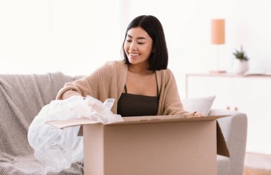 İnternetten alışveriş yaptıktan sonra paketleri açan gülümseyen Asyalı kadın.