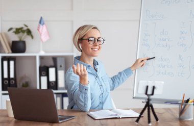 Genç mutlu öğretmen evde İngilizce dersi veriyor, laptopun önünde yabancı dil çalışıyor.