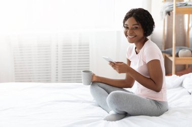 Yatakta cep telefonu kullanan neşeli siyahi kadın.