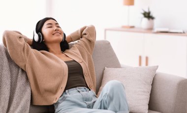 Sakin Asyalı kadın kulaklık takıp müzik dinliyor.