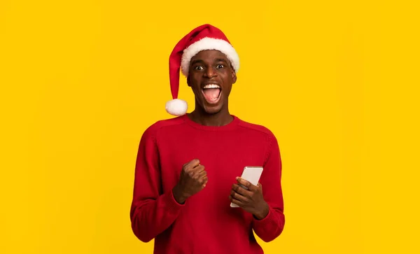 Chico Negro Emocionado en Santa Claus Sombrero Celebrando el Éxito Con Smartphone — Foto de Stock