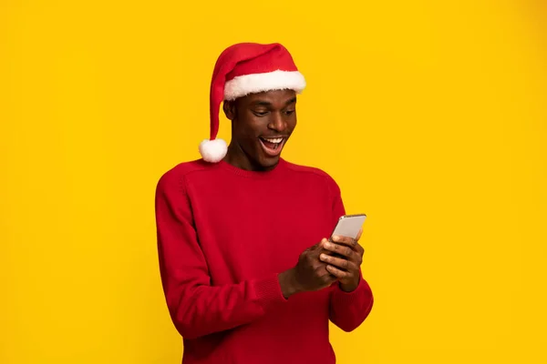 Chico negro sorprendido en navidad sombrero de santa mirando la pantalla del teléfono inteligente — Foto de Stock