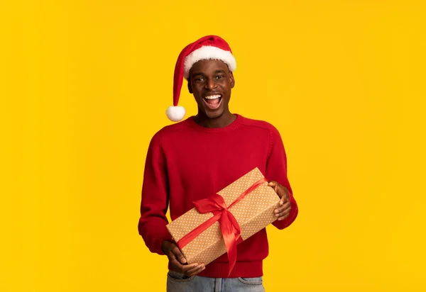 休日を楽しむ。サンタ帽子保持クリスマスプレゼントボックスで陽気な黒人男性 — ストック写真