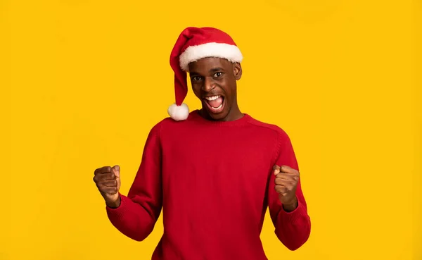 Navidad, por fin. Chico negro lleno de alegría en Santa Sombrero celebrando el éxito, apretando los puños — Foto de Stock