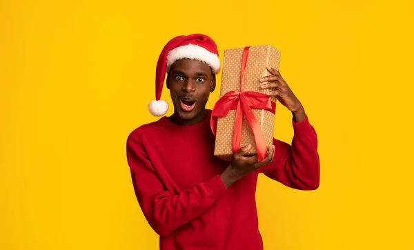 Prezent świąteczny. Zaskoczony czarny facet w Santa kapelusz gospodarstwa Christmas Gift Box — Zdjęcie stockowe