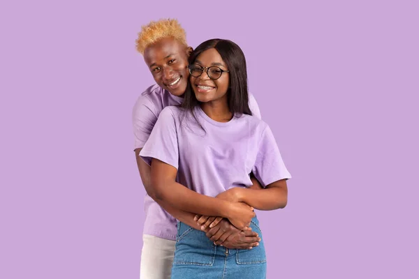 Millennial schwarzer Kerl umarmt seine schöne Freundin in Brille auf fliederfarbenem Hintergrund — Stockfoto