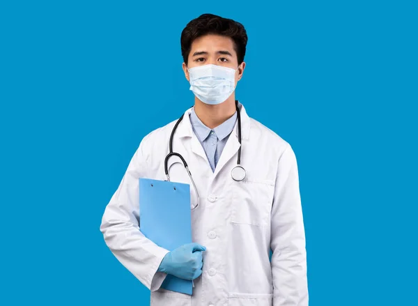 Ásia cara no médico máscara segurando pasta posando no estúdio — Fotografia de Stock