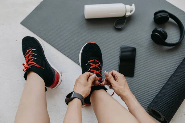 Спортивная женщина завязывает шнурки на ботинках, делая перерыв между тренировками дома — стоковое фото