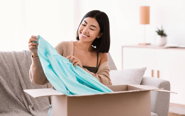 Gelukkig aziatische dame uitpakken kleding thuis — Stockfoto