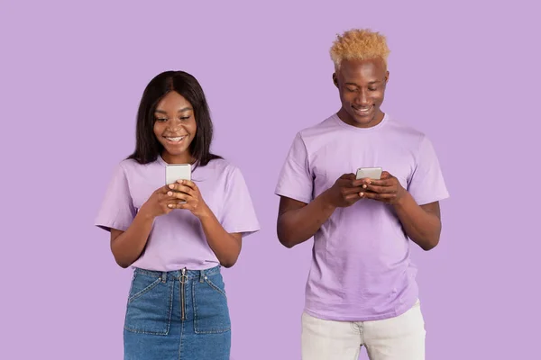 Porträt eines jungen schwarzen Paares mit Smartphones vor fliederfarbenem Studiohintergrund — Stockfoto