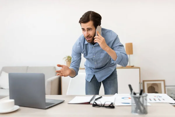 Δυσαρεστημένος επιχειρηματίας μιλώντας στο κινητό τηλέφωνο έχοντας πρόβλημα με τον υπολογιστή στο γραφείο — Φωτογραφία Αρχείου