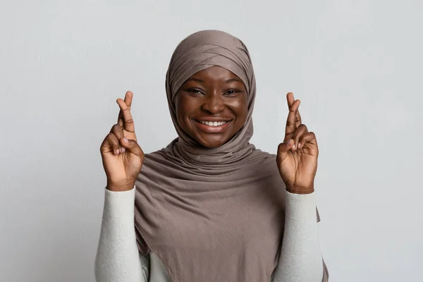 Snälla, snälla, snälla. Närbild porträtt av drömmande svart muslim flicka i hijab korsning fingrar, att önska, över gul bakgrund — Stockfoto
