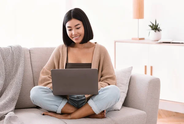 Asian woman sitting on couch and working on laptop — Stock Photo, Image