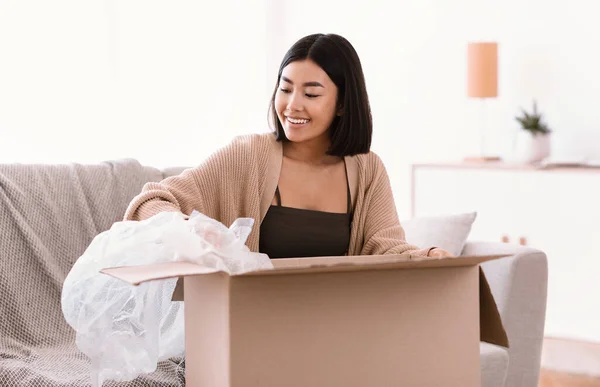 Lächelnde Asiatin packt nach Online-Einkauf Paket aus — Stockfoto