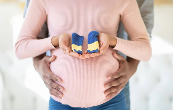 Przycięty widok czarnej kobiety w ciąży i jej męża z maleńkimi skarpetkami, zbliżenie — Zdjęcie stockowe