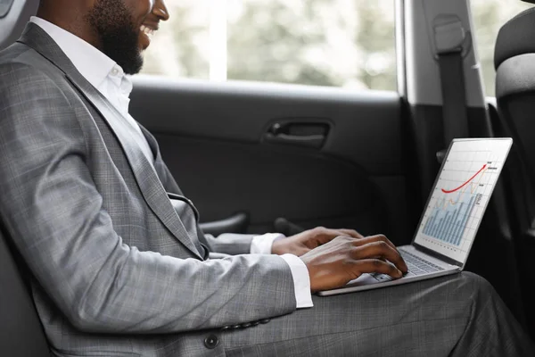 Oigenkännlig svart affärsman som arbetar på bärbar dator i bilen — Stockfoto