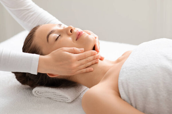 Joyful young woman relaxing during face lifting massage