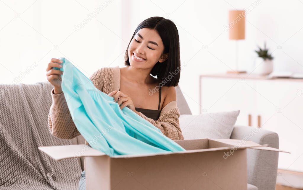 Happy asian lady unpacking clothes at home