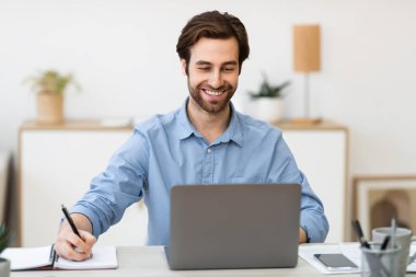 Ofiste çalışan neşeli iş adamı not alıyor.