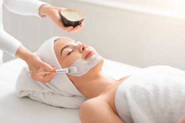 Kadın yüzüne beyaz çamur maskesi takan bir güzellik uzmanı.