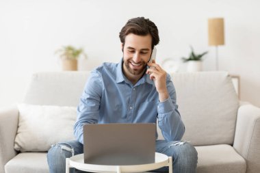 Cep telefonuyla konuşan adam bilgisayarını kullanarak evden uzakta çalışıyor.