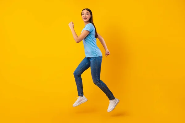 Šťastná dáma skákání a běh přes žluté studio zeď — Stock fotografie