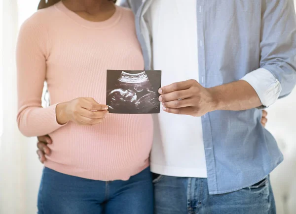 Vista ritagliata della giovane coppia incinta che tiene la foto del loro bambino non ancora nato in casa, da vicino — Foto Stock