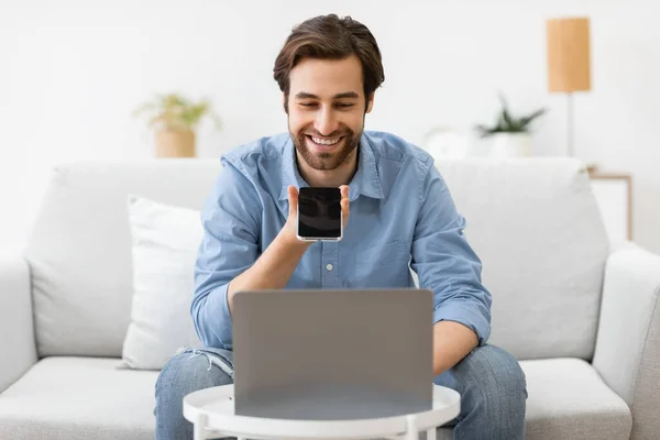 स्मार्टफोनवर लॅपटॉप घरातील बसून लाऊडस्पीकर मोड वापरत माणूस — स्टॉक फोटो, इमेज