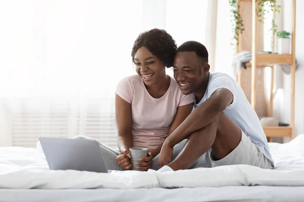 Ευτυχισμένο μαύρο ζευγάρι κάθεται στο κρεβάτι, βλέποντας ταινία στο laptop — Φωτογραφία Αρχείου