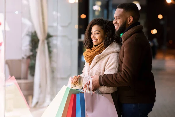 Feliz pareja negra con bolsas de compras mirando a la ventana del centro comercial —  Fotos de Stock