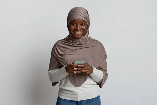 Modern fekete iszlám nő Hidzsábon okostelefonnal és mosollyal a kamerában — Stock Fotó