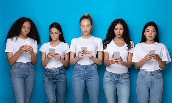 Cinq femmes Milléniales Diverses utilisant des téléphones debout sur fond bleu — Photo