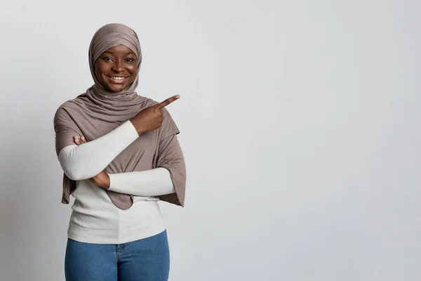 Koukni na tohle. Usmívající se africká muslimská dáma ukazující na kopírovací prostor s prstem — Stock fotografie