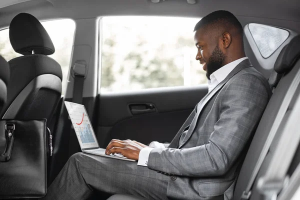 Leende svart kille affärsman som arbetar på laptop i bilen — Stockfoto