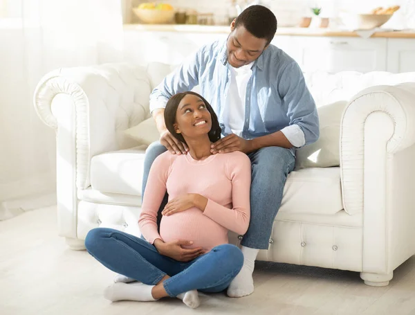 Teljes hosszúságú portré egy jóképű fekete férfiról, aki otthon masszírozza terhes feleségét. — Stock Fotó