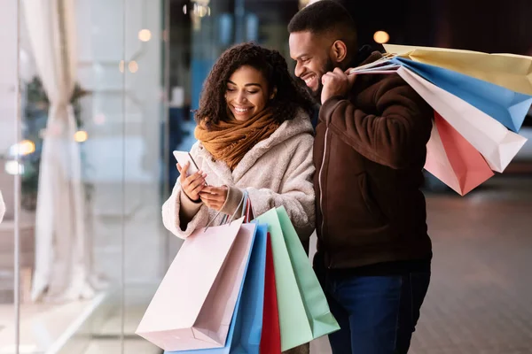 Portret van gelukkig afro paar met behulp van telefoon met boodschappentassen — Stockfoto