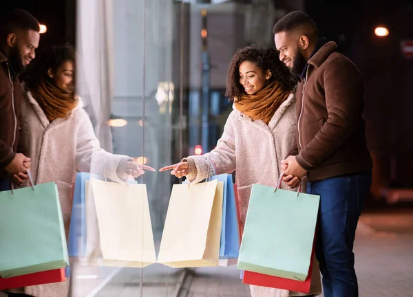 Happy black couple with shopping bags looking at mall window — Stock Photo, Image